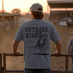 Man wearing a 'Outback King' t-shirt with a horse graphic at sunset in a rural setting.