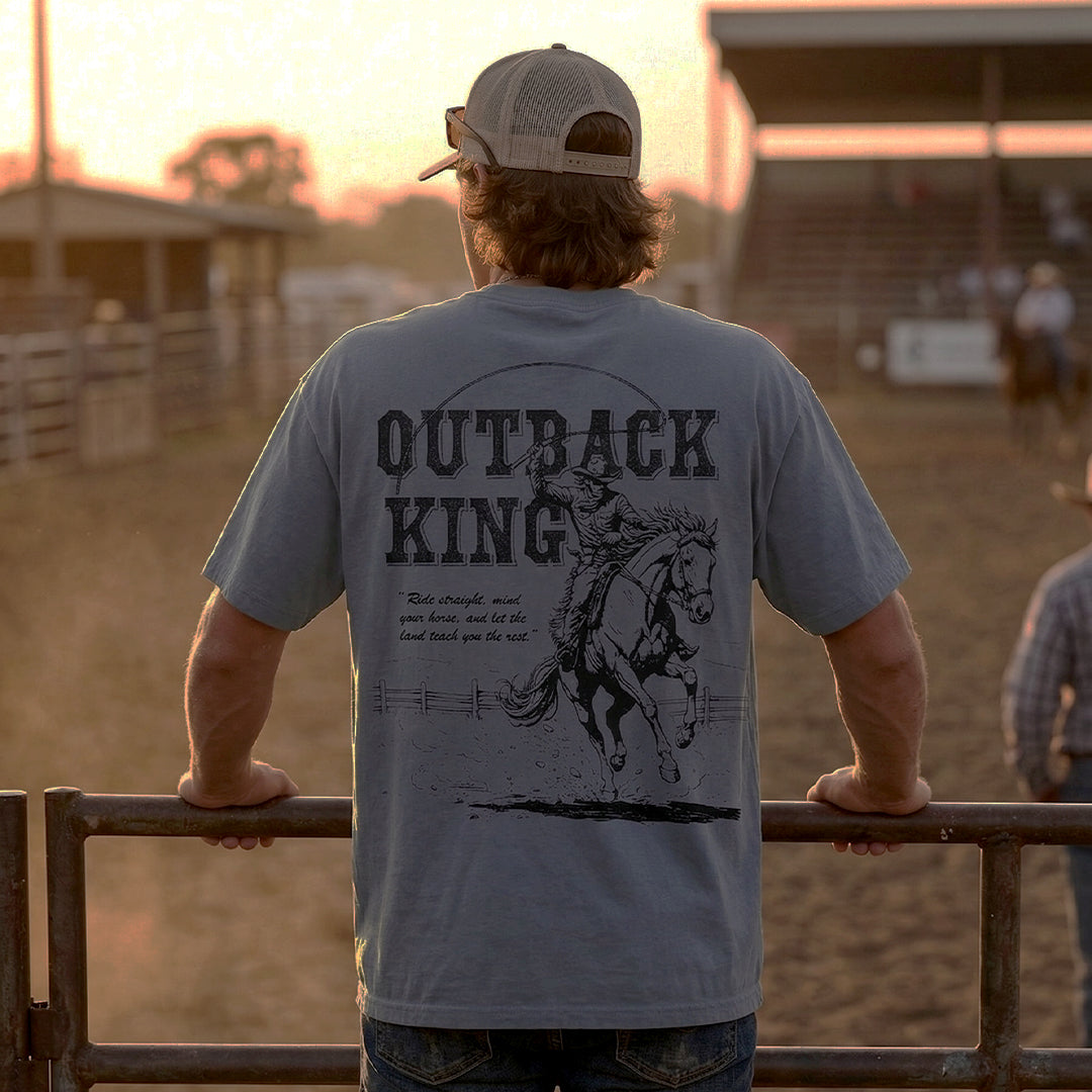 Man wearing a 'Outback King' t-shirt with a horse graphic at sunset in a rural setting.